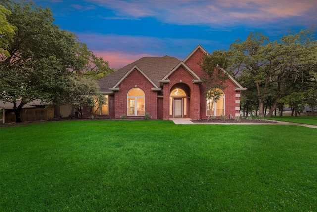 view of front of home with roof with shingles, brick siding, and a front lawn