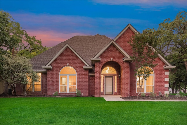 view of front of house with brick siding, roof with shingles, and a front yard
