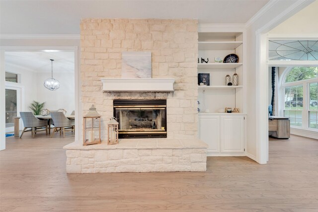 living room featuring a stone fireplace, light wood-type flooring, ornamental molding, and a notable chandelier