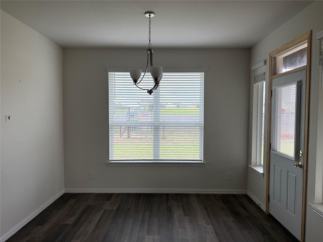 unfurnished dining area with a healthy amount of sunlight, baseboards, dark wood-style floors, and a notable chandelier