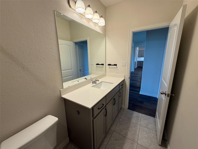 bathroom featuring vanity, toilet, a textured wall, and tile patterned flooring