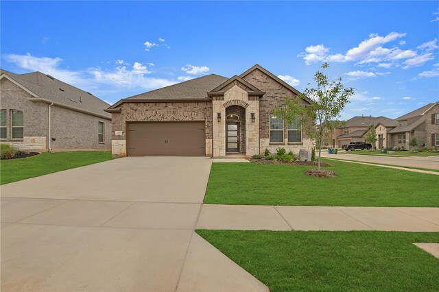 10337 Geode St, Aubrey, TX 76227 - french country style house with an attached garage, concrete driveway, a front lawn, brick siding, and roof with shingles