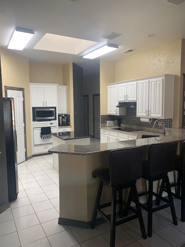 6001 Rock Cv, Flower Mound, TX 75028 - kitchen with black appliances, a peninsula, backsplash, a breakfast bar, and light tile patterned floors