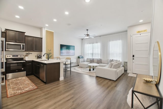 kitchen with a peninsula, a sink, stainless steel appliances, open floor plan, and dark brown cabinetry