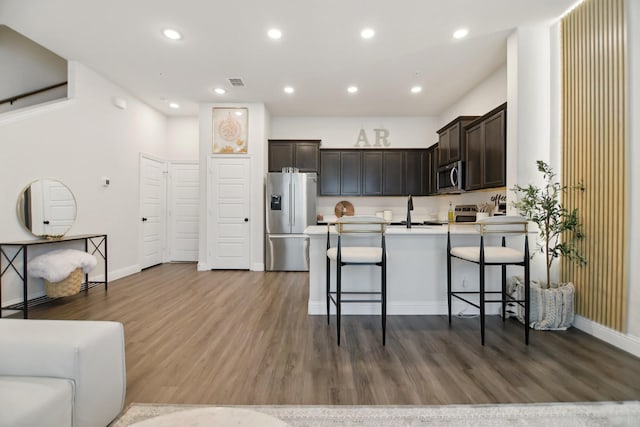 kitchen with a peninsula, dark brown cabinets, dark wood-type flooring, appliances with stainless steel finishes, and recessed lighting