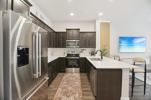 kitchen featuring dark brown cabinets, a sink, a peninsula, wood finished floors, and appliances with stainless steel finishes