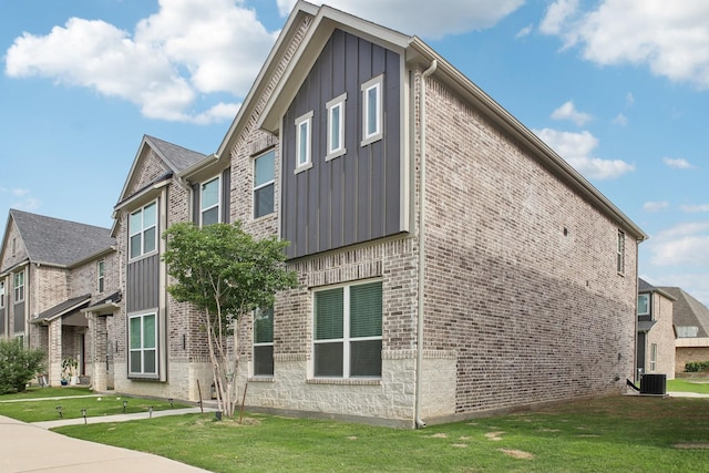 view of side of property featuring a lawn, board and batten siding, brick siding, and central air condition unit