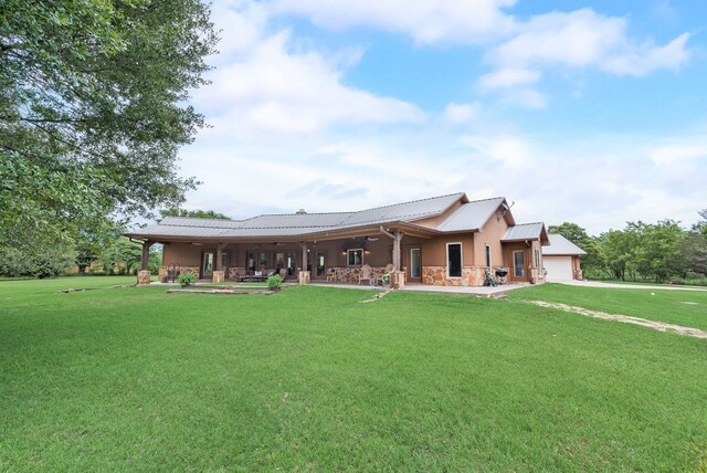 rear view of property with a yard, a garage, metal roof, and stone siding