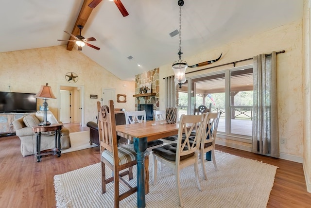 dining space featuring visible vents, light wood finished floors, beamed ceiling, a ceiling fan, and a stone fireplace