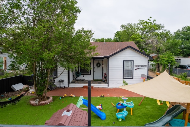 1100 Hillburn Dr, Dallas, TX 75217 - view of front of house with a front yard, a shingled roof, a playground, and fence