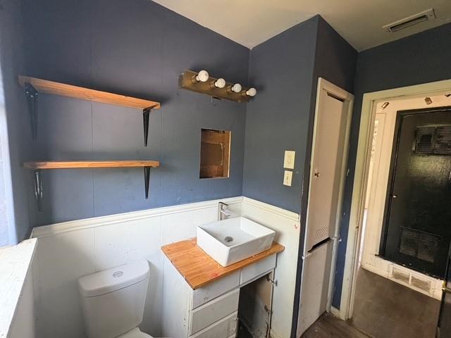 half bathroom with vanity, toilet, visible vents, and wood finished floors