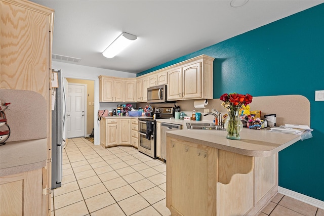 101 Remington Trl, Longview, TX 75604 - kitchen featuring a peninsula, light tile patterned floors, a sink, light brown cabinetry, and appliances with stainless steel finishes