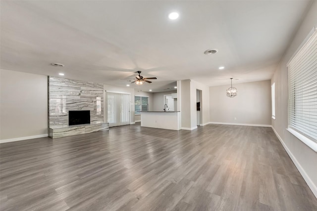 unfurnished living room featuring a fireplace, a ceiling fan, dark wood finished floors, recessed lighting, and a chandelier