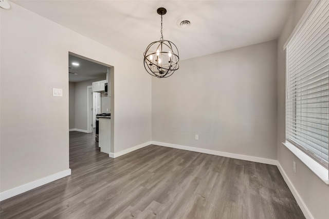 unfurnished dining area with dark wood finished floors, a chandelier, and baseboards