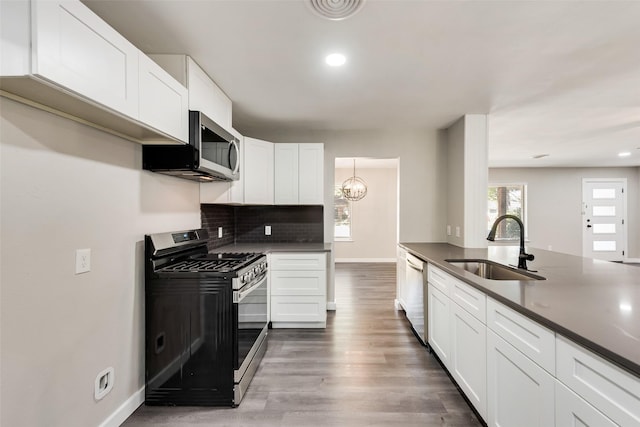 kitchen featuring stainless steel appliances, a sink, dark countertops, decorative backsplash, and white cabinetry