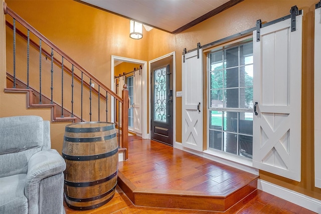 entryway featuring a barn door, stairway, baseboards, crown molding, and hardwood / wood-style floors