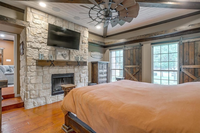 bedroom with wooden ceiling, a fireplace, a barn door, and wood finished floors