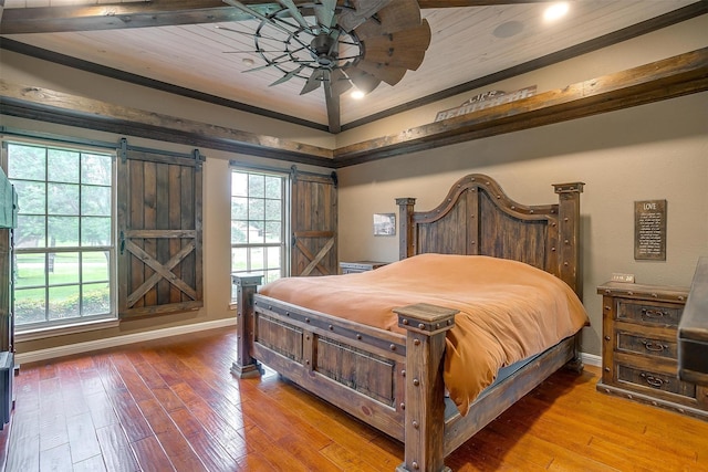bedroom featuring a ceiling fan, wood-type flooring, crown molding, a barn door, and baseboards