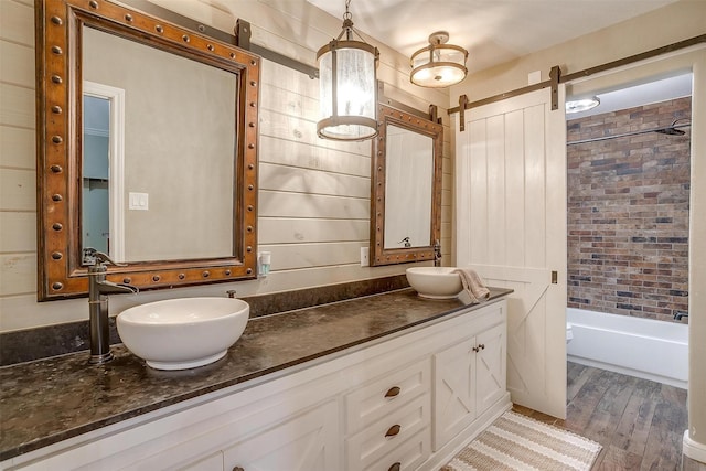 full bath with double vanity, washtub / shower combination, wood finished floors, and a sink