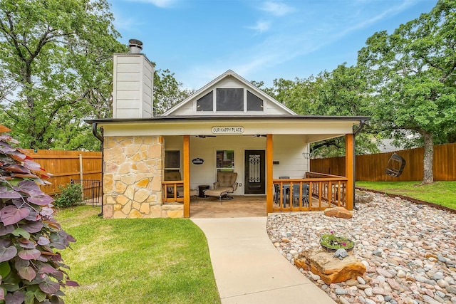 view of front of house with a fenced backyard, stone siding, a front lawn, and a chimney