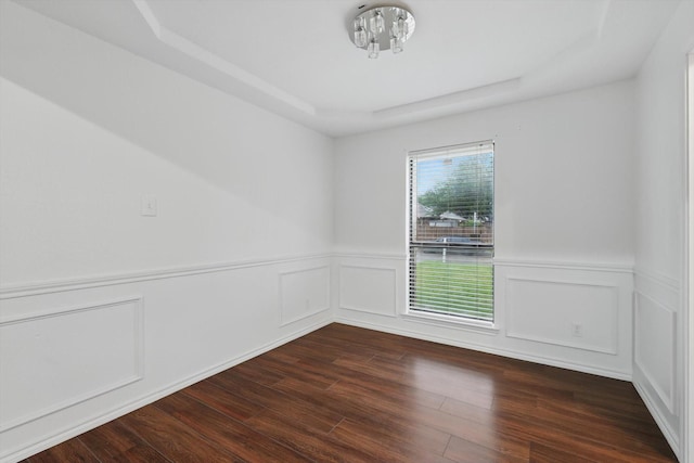 empty room featuring wainscoting, a decorative wall, a tray ceiling, and dark wood-style floors