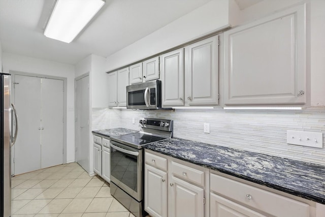 kitchen featuring light tile patterned flooring, dark stone counters, white cabinetry, tasteful backsplash, and appliances with stainless steel finishes