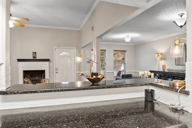 703 Trinidad Dr, Grand Prairie, TX 75052 - kitchen featuring a textured ceiling, crown molding, a brick fireplace, a ceiling fan, and dark stone countertops