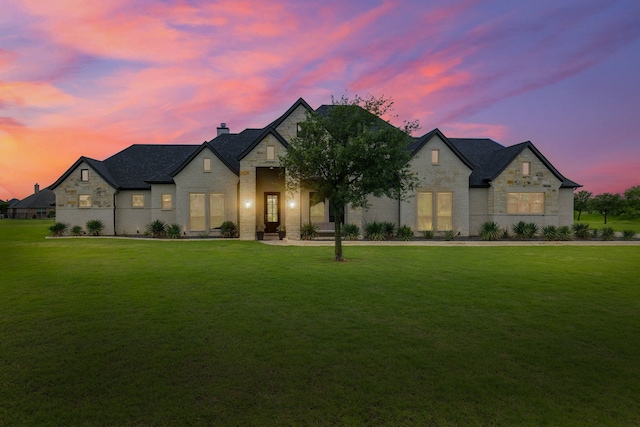 french country home featuring brick siding, a chimney, stone siding, and a front yard
