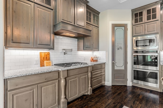 kitchen featuring glass insert cabinets, light stone counters, stainless steel appliances, tasteful backsplash, and dark wood-style floors