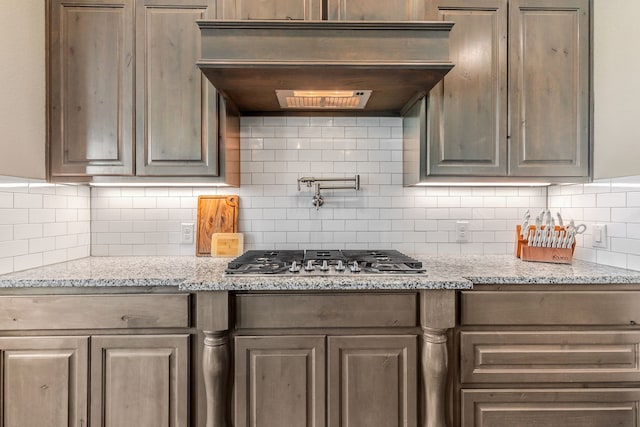 kitchen featuring custom exhaust hood, decorative backsplash, stainless steel gas cooktop, and light stone counters
