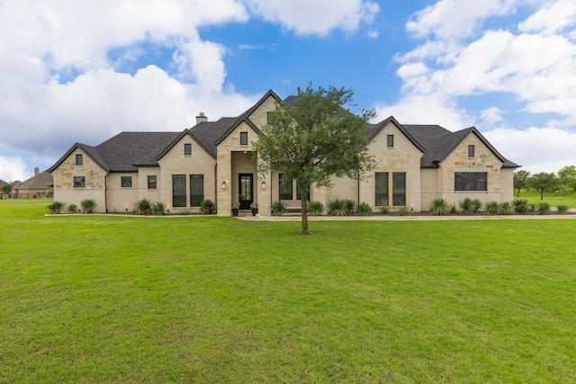french country inspired facade featuring stone siding, brick siding, a chimney, and a front yard