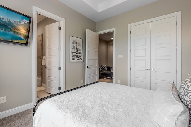 carpeted bedroom with a closet, ensuite bathroom, and baseboards