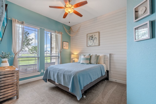 carpeted bedroom featuring baseboards, wooden walls, and a ceiling fan