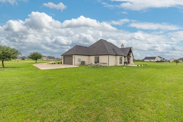 back of house featuring a yard, a chimney, an attached garage, and concrete driveway