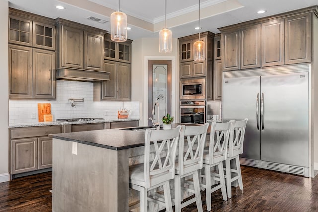 kitchen featuring a sink, built in appliances, ornamental molding, visible vents, and decorative backsplash