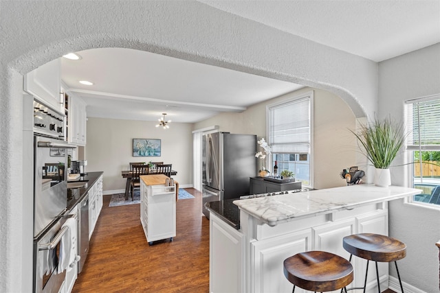 2512 Halloran St, Fort Worth, TX 76107 - kitchen featuring dark wood finished floors, white cabinetry, a kitchen island, arched walkways, and stainless steel appliances