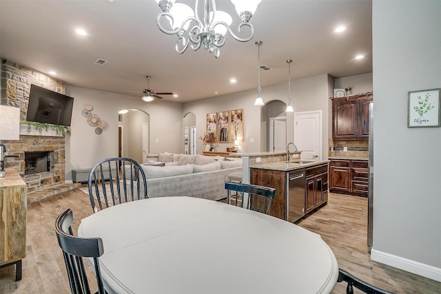 dining area with ceiling fan with notable chandelier, recessed lighting, a fireplace, light wood-style flooring, and arched walkways