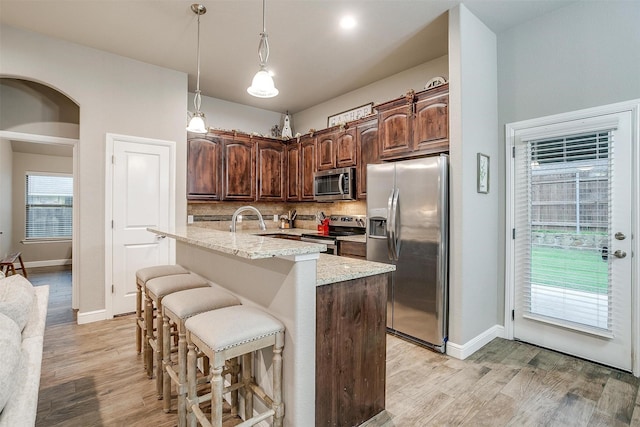 kitchen featuring appliances with stainless steel finishes, decorative backsplash, light stone counters, and light wood-style floors