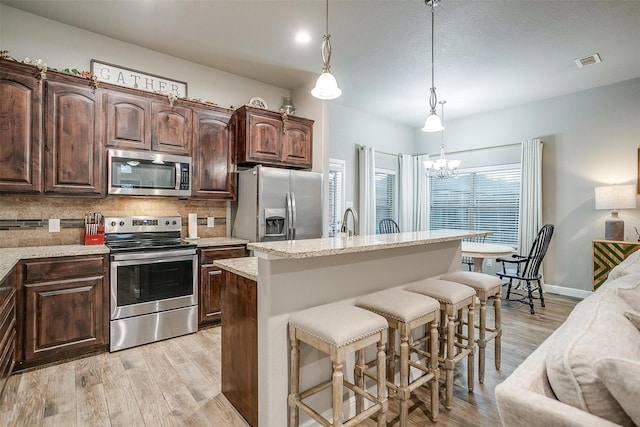 kitchen with a breakfast bar, light wood-style flooring, backsplash, a notable chandelier, and appliances with stainless steel finishes