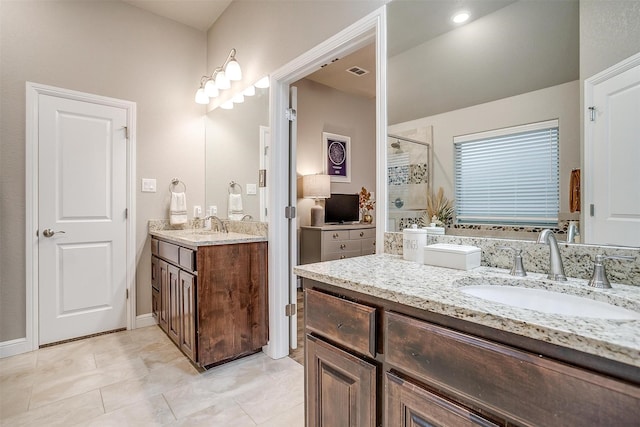 full bath featuring a sink, two vanities, tiled shower, and visible vents