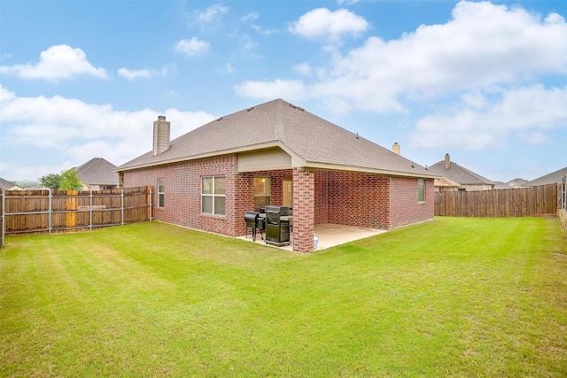 rear view of house with a patio, a chimney, a lawn, a fenced backyard, and brick siding