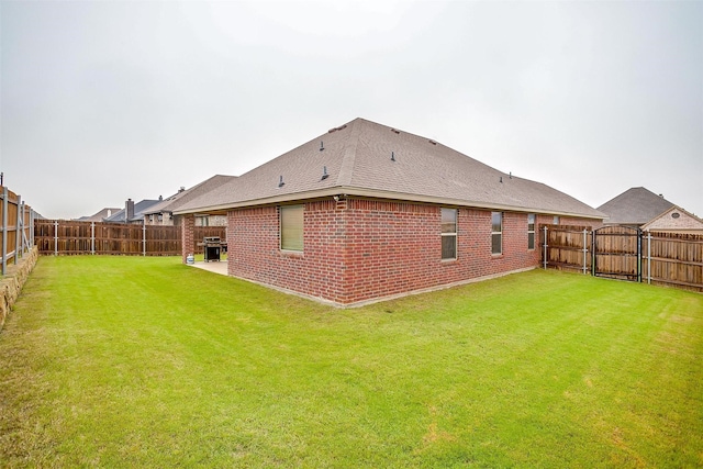 rear view of house with a lawn, a patio, brick siding, and a fenced backyard