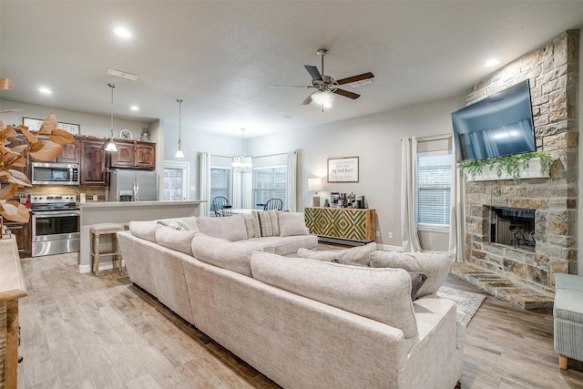 living area featuring a ceiling fan, a stone fireplace, light wood finished floors, and recessed lighting