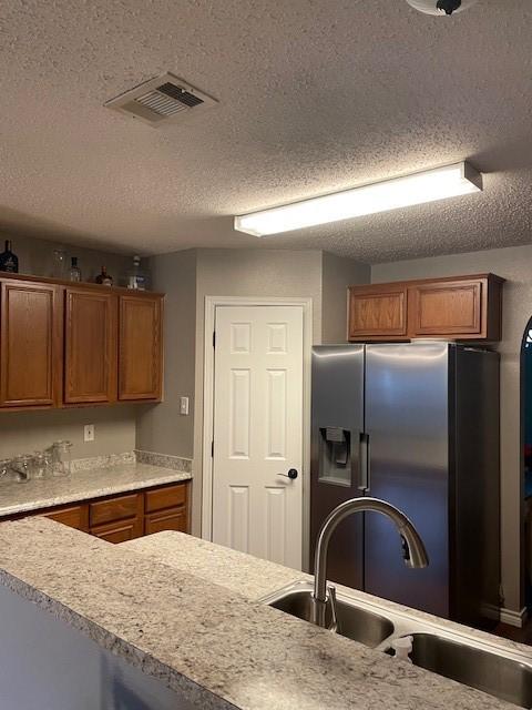 502 Blueberry Hill Ln, Mansfield, TX 76063 - kitchen with a sink, stainless steel fridge, brown cabinetry, a textured ceiling, and light countertops