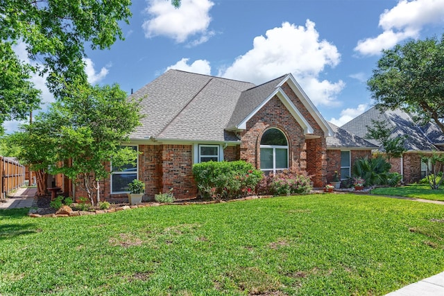 ranch-style house featuring a shingled roof, brick siding, fence, and a front yard