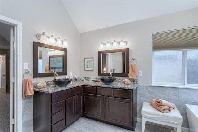 bathroom featuring a sink, double vanity, lofted ceiling, and a washtub