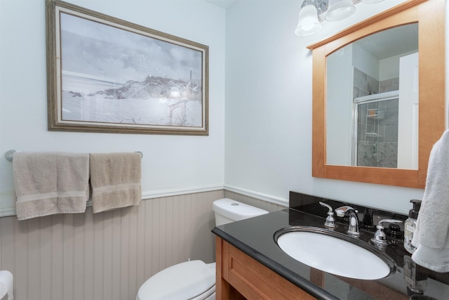 bathroom featuring vanity, wainscoting, toilet, and a stall shower