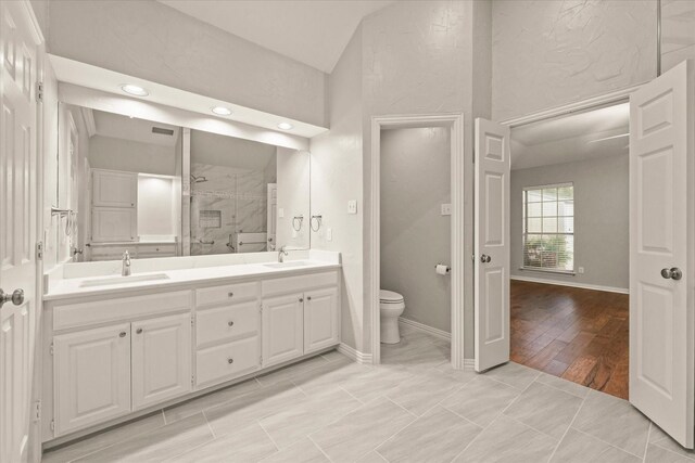 bathroom featuring toilet, a shower stall, double vanity, lofted ceiling, and recessed lighting