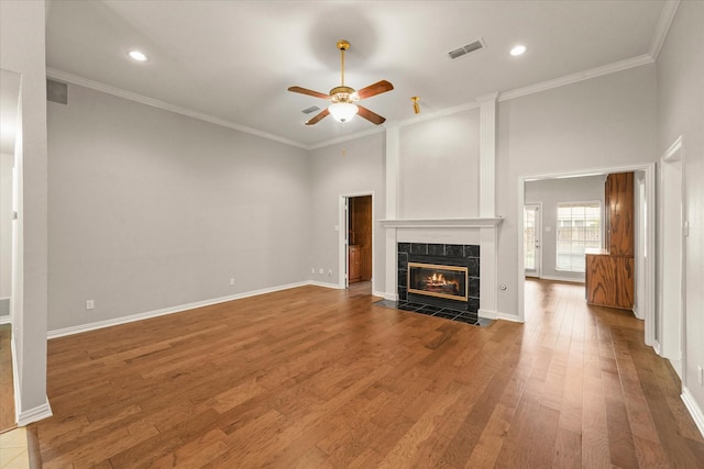unfurnished living room with ceiling fan, a tiled fireplace, wood finished floors, crown molding, and recessed lighting