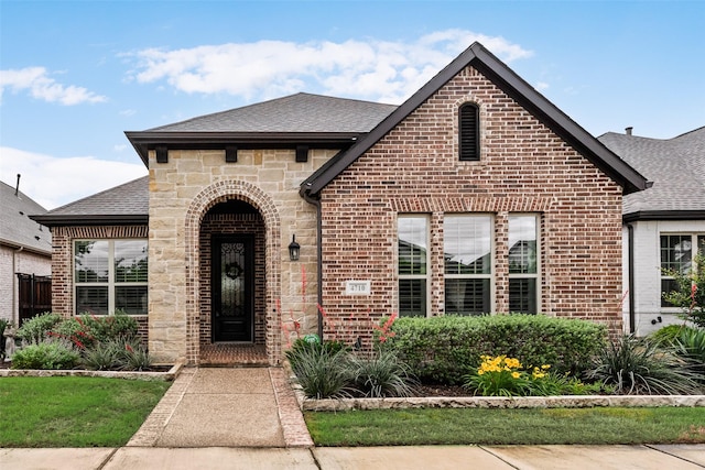 french country style house featuring roof with shingles, stone siding, and brick siding